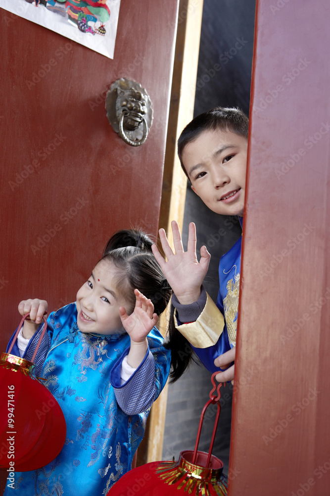 一个小男孩和一个小女孩拿着灯笼站在他们传统的开放门口挥手