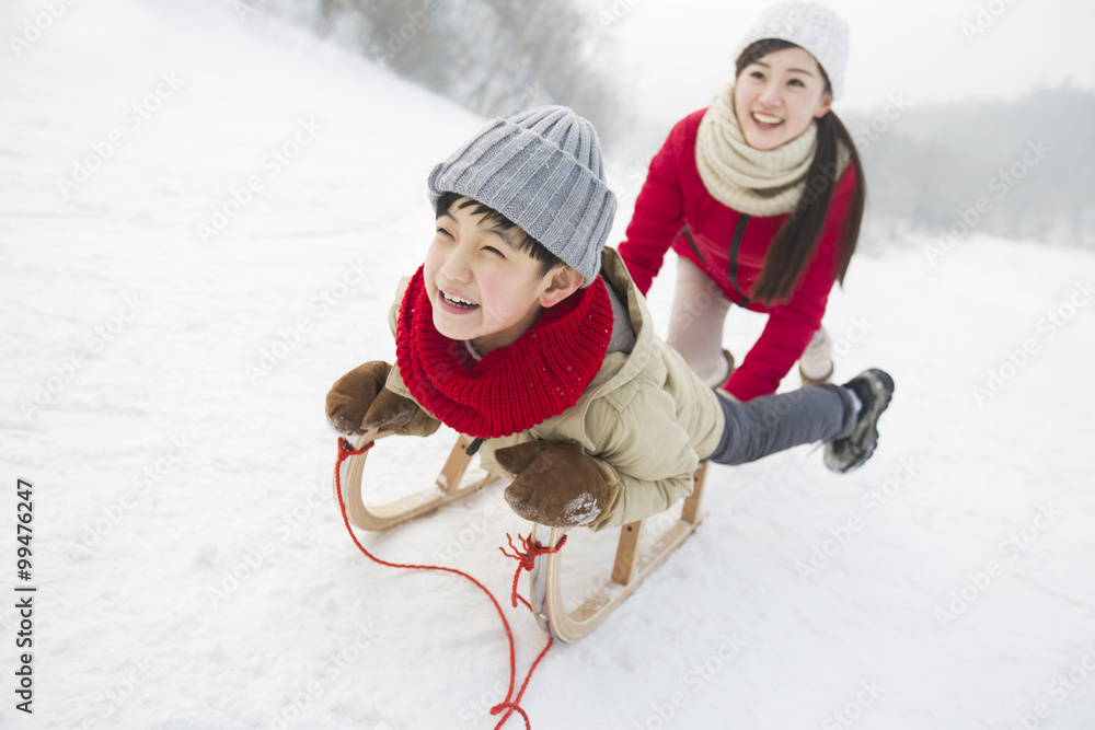 Young mother pulling son on sled