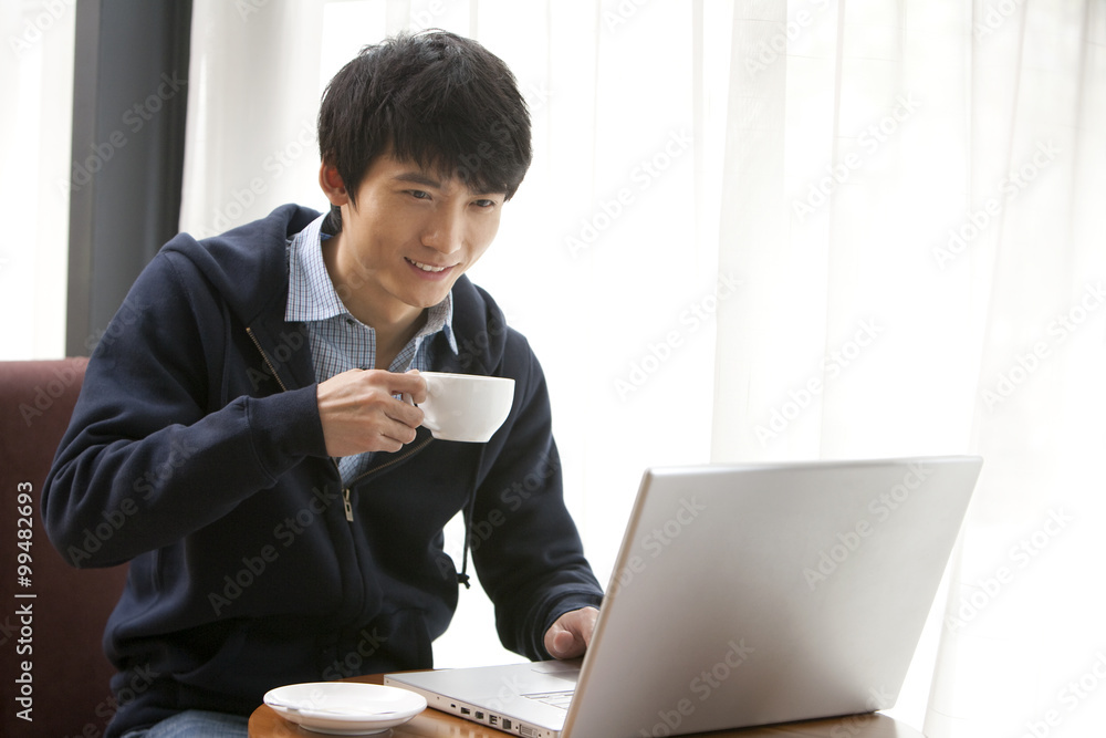 一个年轻人在咖啡馆用笔记本电脑喝咖啡