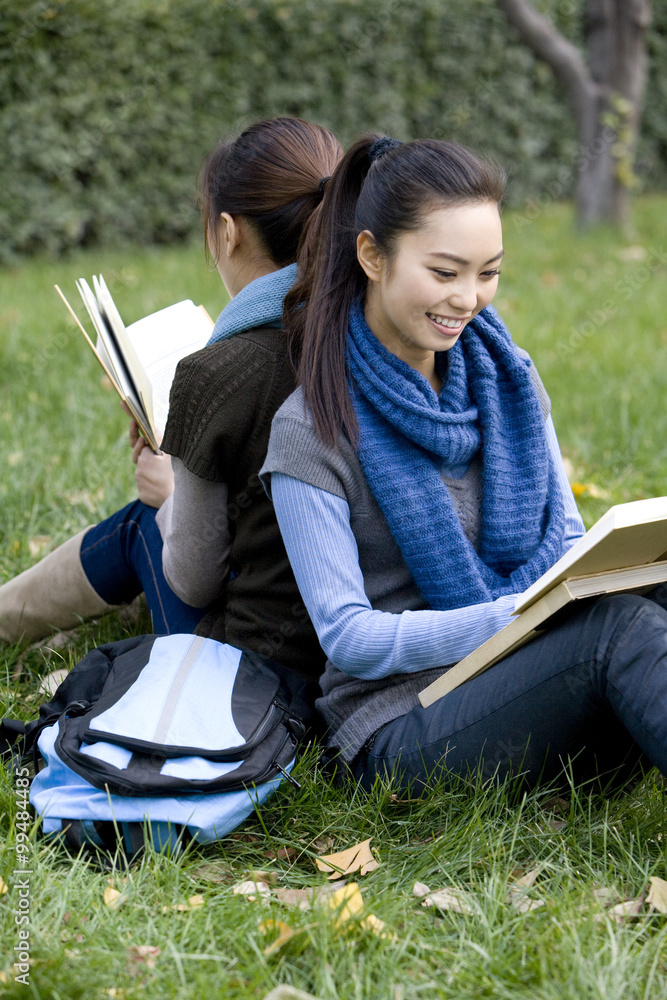 两个朋友背靠背坐在草地上学习