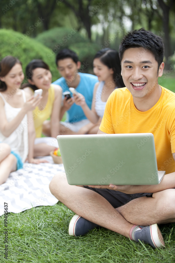 年轻人在草地上使用电脑，背景是朋友