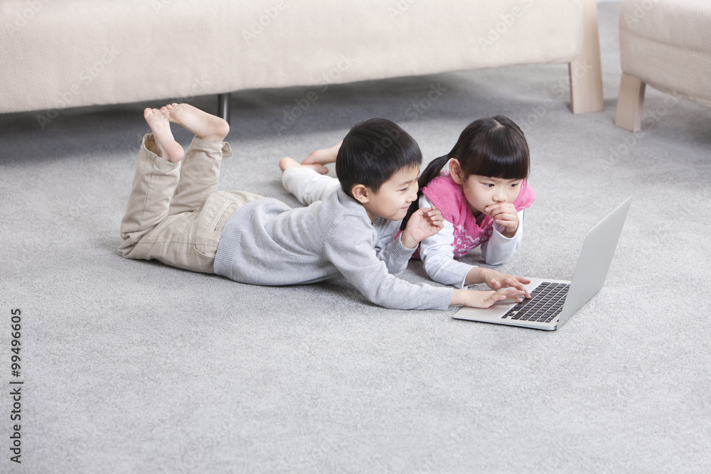 兴奋的男孩和女孩在地板上使用笔记本电脑