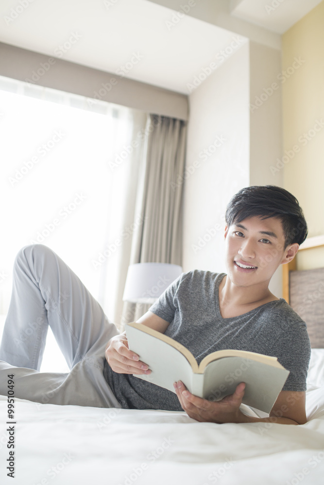 Young man reading book on bed