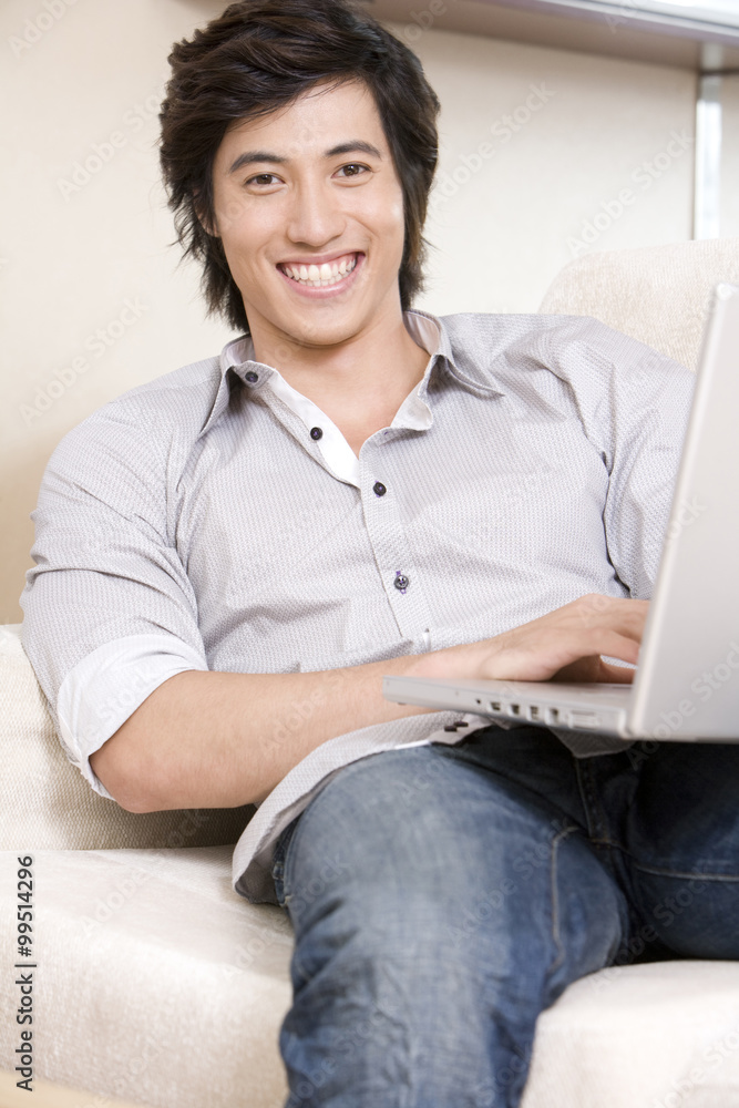 亚洲男子拿着笔记本电脑坐在沙发上