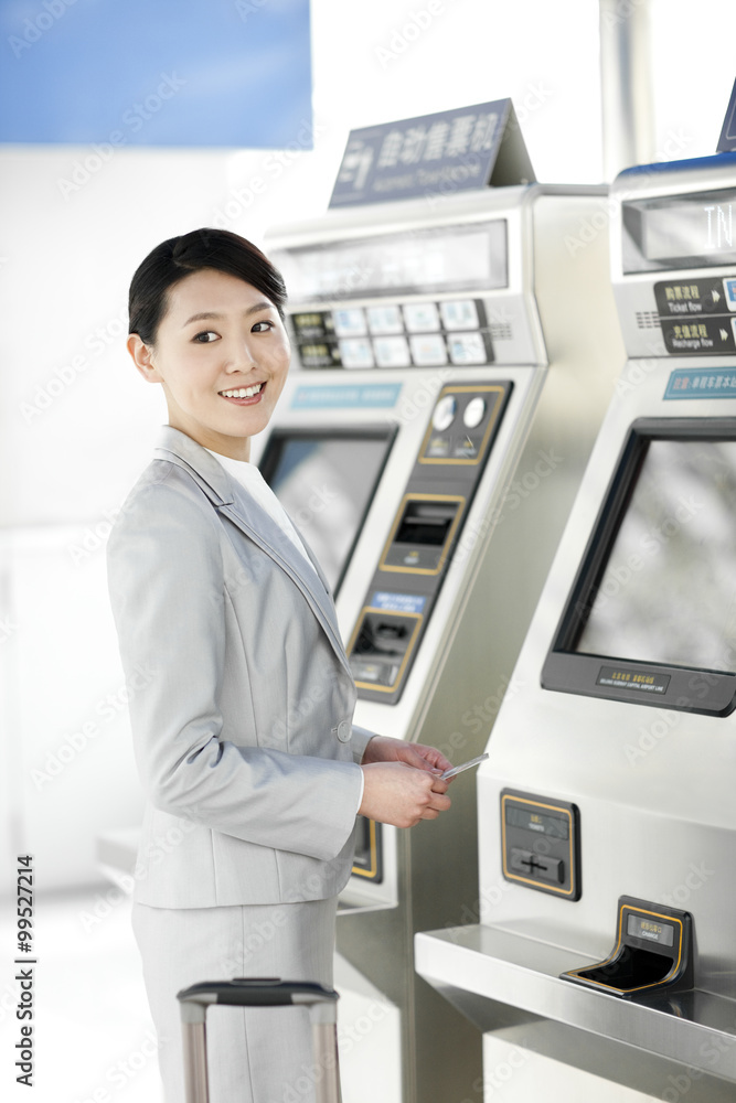 年轻女商人在地铁站使用自动售票机