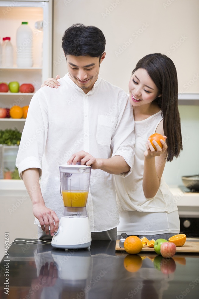 Young couple using juicer in kitchen