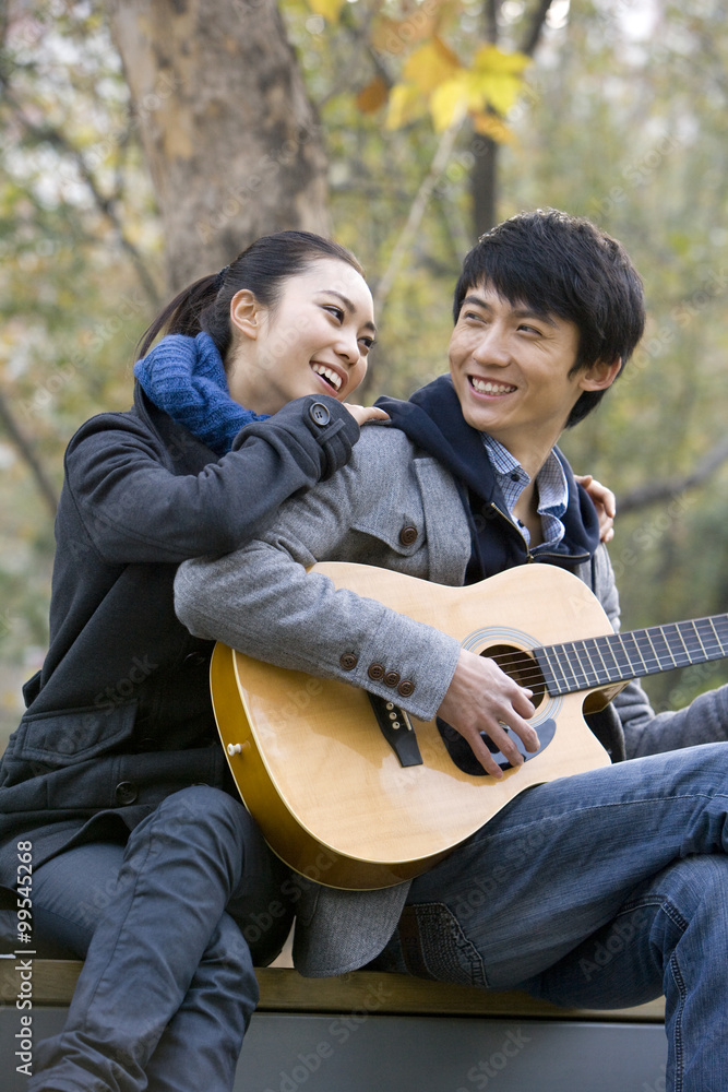 一个年轻人弹吉他，他的女朋友深情地靠在他身上