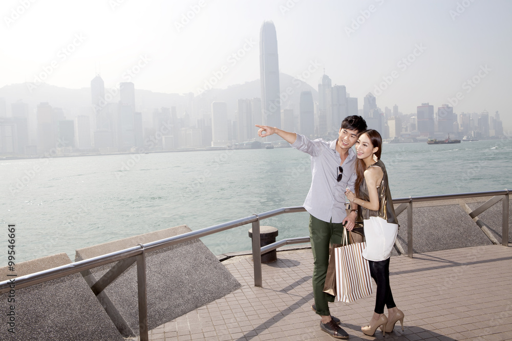 幸福的年轻夫妇带着购物袋欣赏香港维多利亚港的壮丽景色