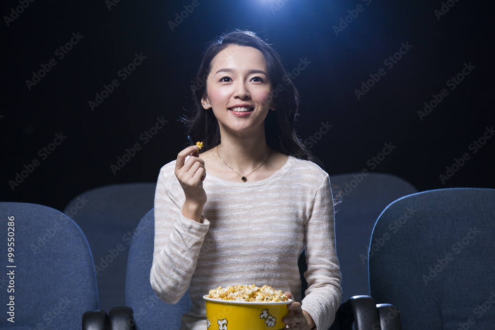 年轻女子手里拿着爆米花在电影院看电影