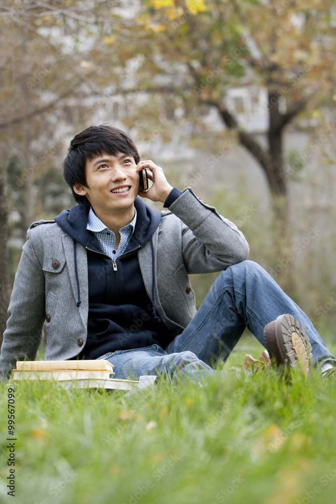 A young man sitting on a grassy area talking on the phone
