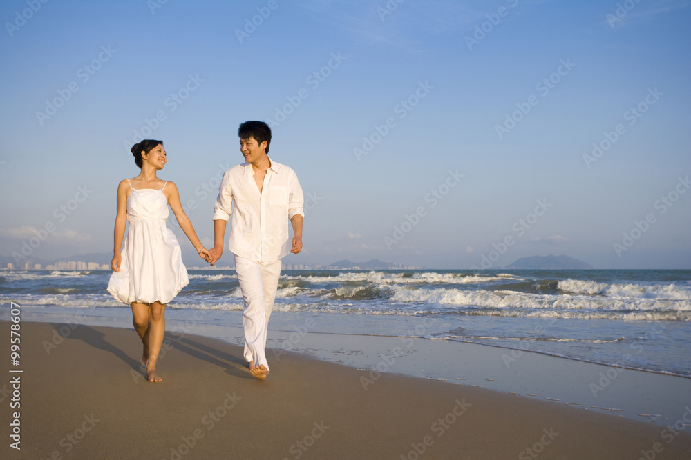一对穿着白色衣服的年轻夫妇沿着海滩散步