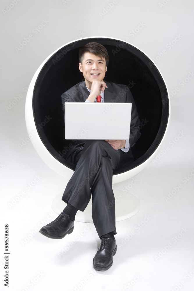 年轻商人在球椅上使用笔记本电脑