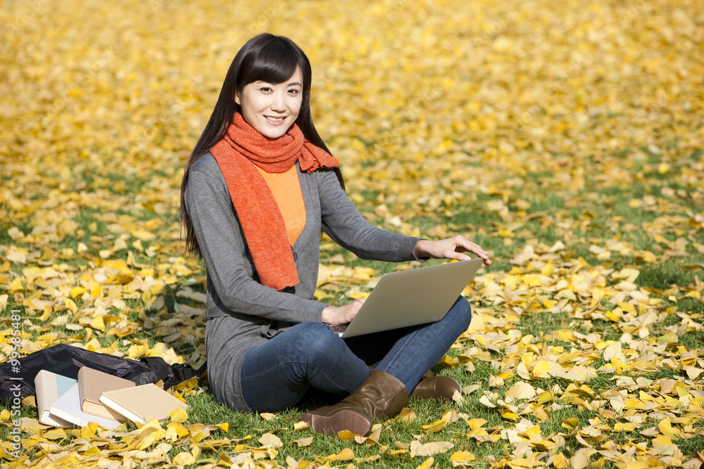 快乐的年轻女人秋天在草坪上用笔记本电脑