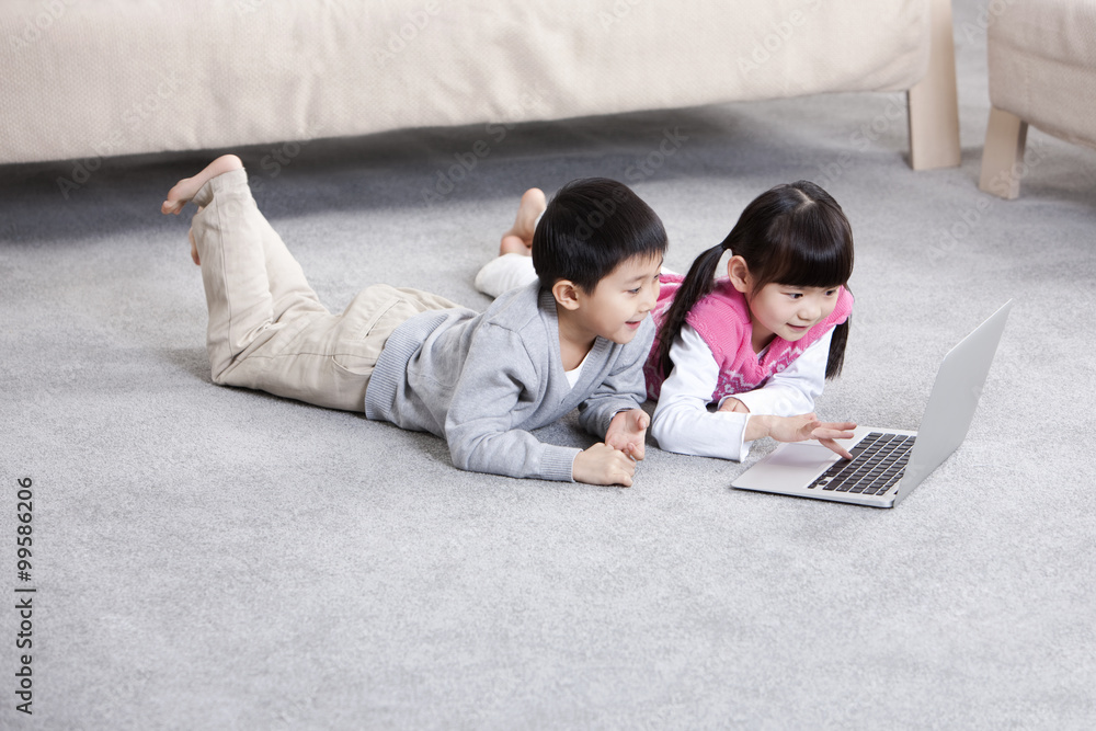 兴奋的男孩和女孩在地板上使用笔记本电脑