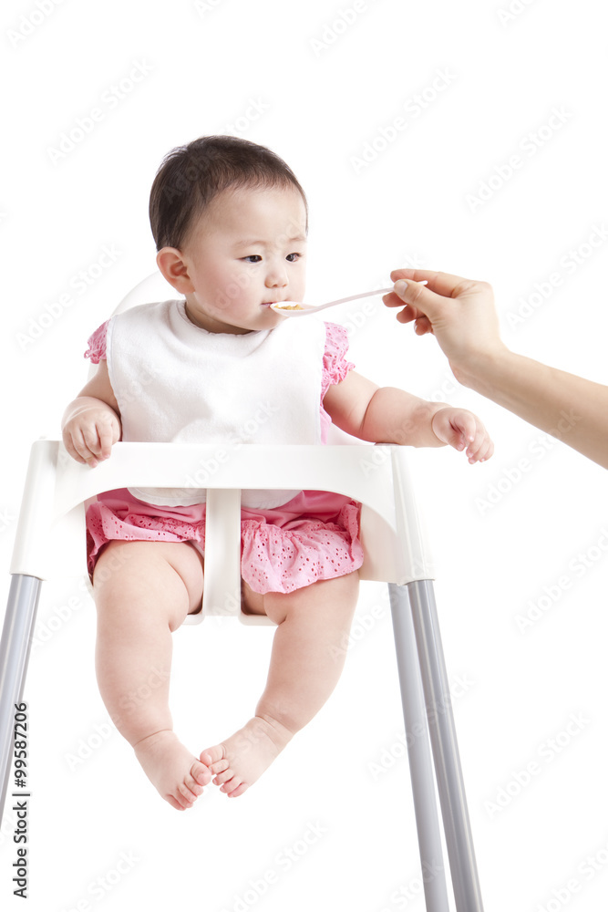 可爱的女婴被喂在婴儿高脚椅上