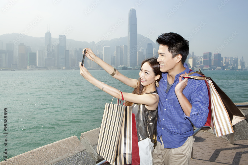 时尚年轻情侣拿着购物袋在香港维多利亚港自拍