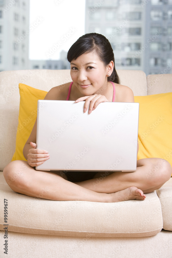 亚洲女人拿着笔记本电脑坐在沙发上