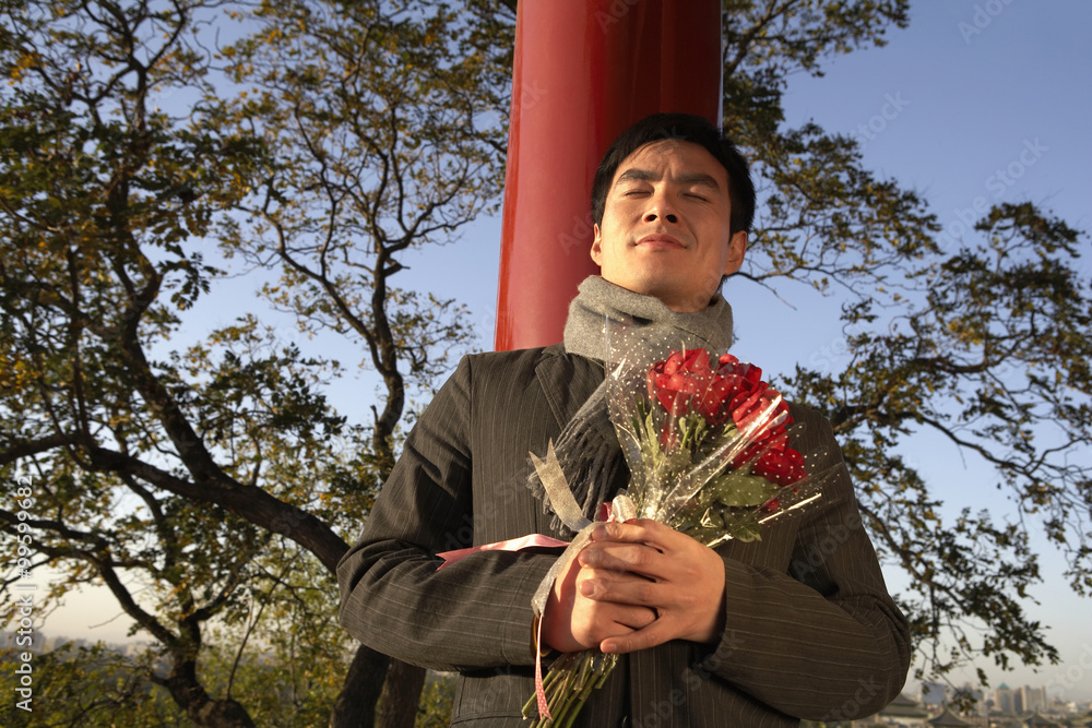 年轻人靠在柱子上，手里拿着一束花
