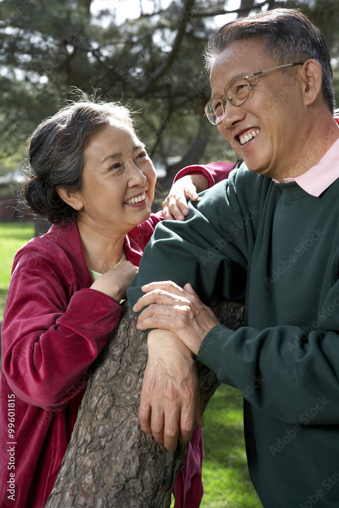 Senior Chinese Couple Leaning On Tree Branch In Park
