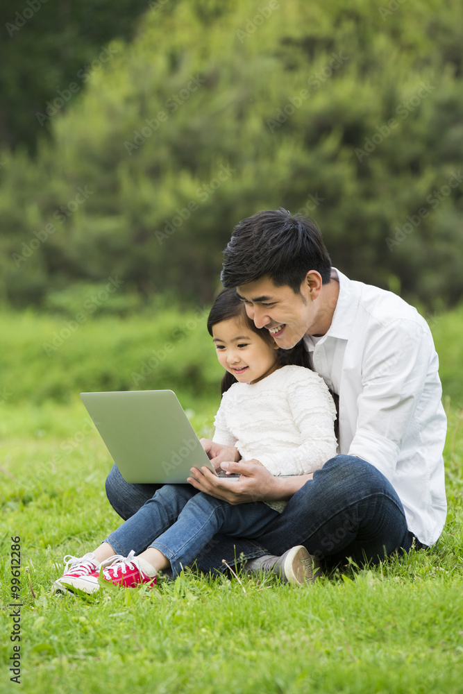 父亲和女儿在草地上使用笔记本电脑