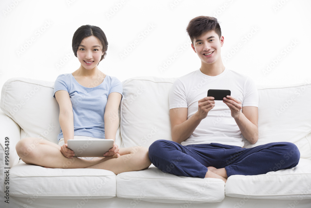 拥有数字平板电脑和智能手机的幸福年轻夫妇