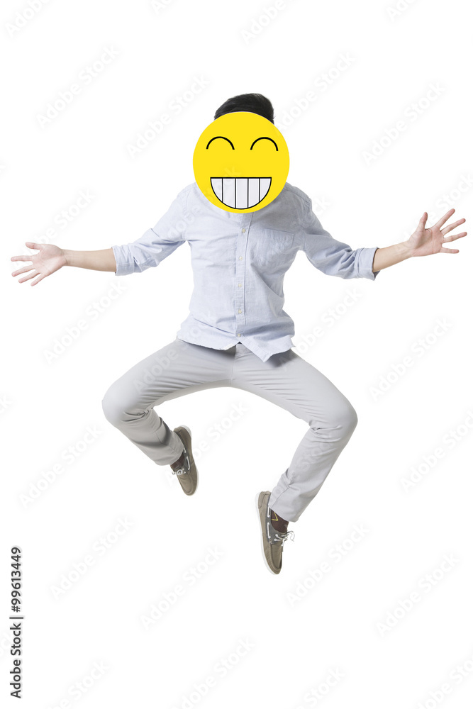 Young man jumping with a happy emoticon face in front of his face