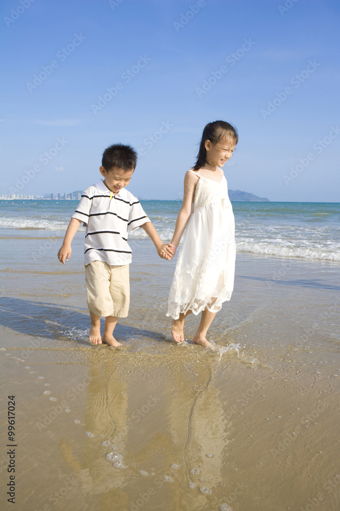 年轻的女孩和男孩沿着海滩散步