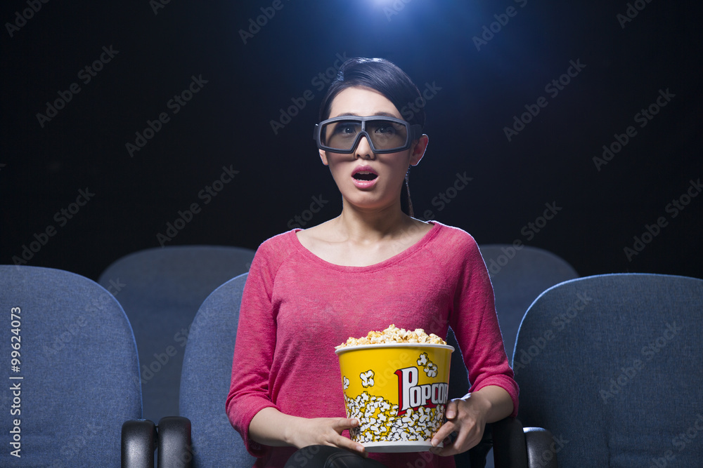 年轻女子在电影院观看3D电影，面部表情惊讶