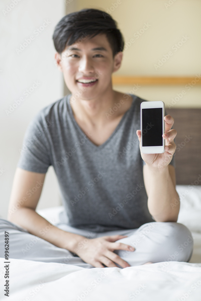年轻人在床上展示智能手机
