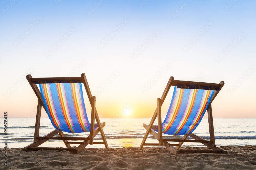 日落时沙滩上的两把躺椅