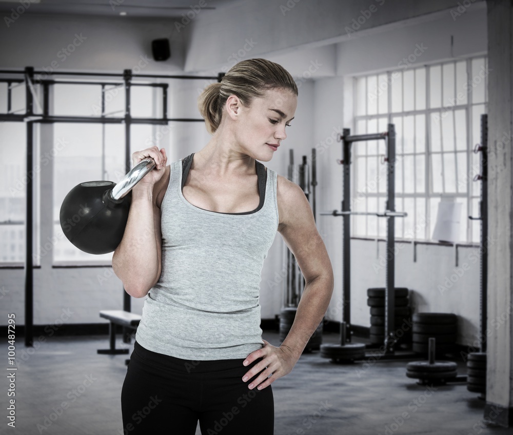 Composite image of serious muscular woman lifting kettlebell 