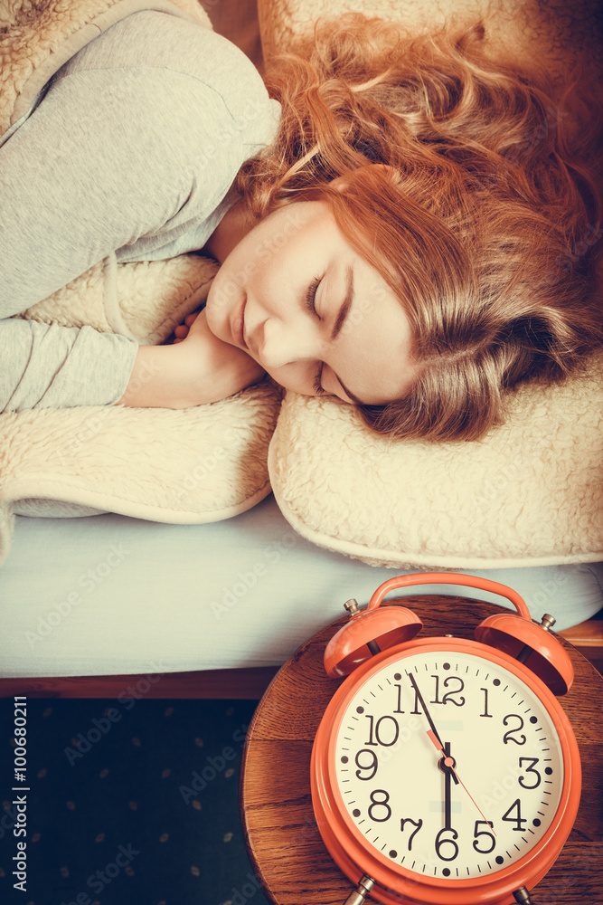 Woman sleeping in bed with set alarm clock.