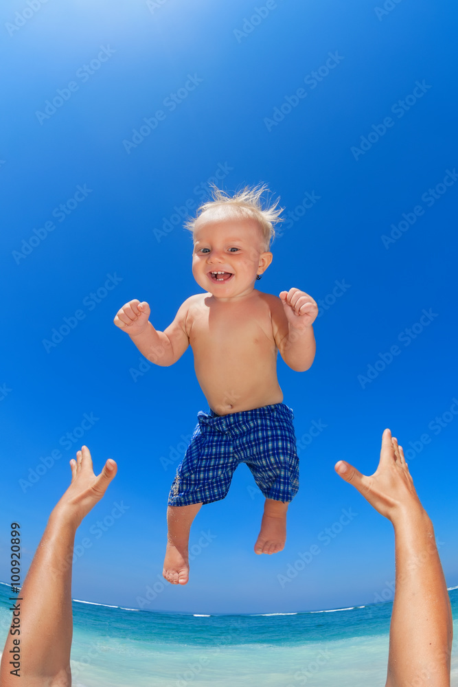 Family swimming fun on white sand sea beach and blue sky - father hands tossing up baby boy into mid