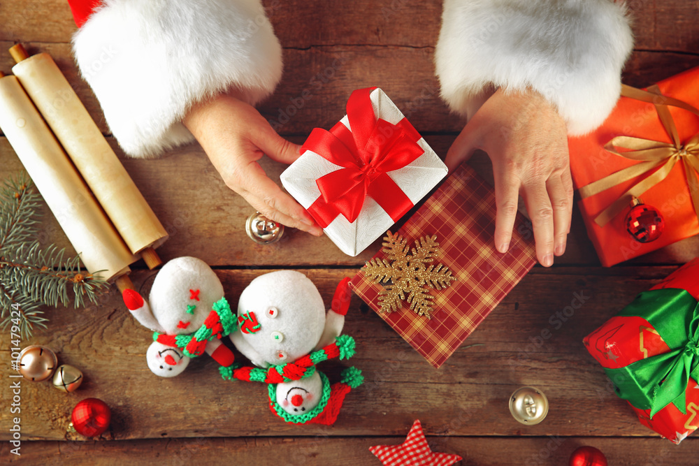 圣诞老人手中的漂亮礼盒和木桌上的圣诞装饰品，特写