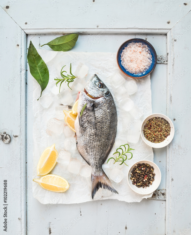 新鲜未煮熟的鲷鱼，配柠檬、香草、冰块和香料，背景为质朴的蓝色木板