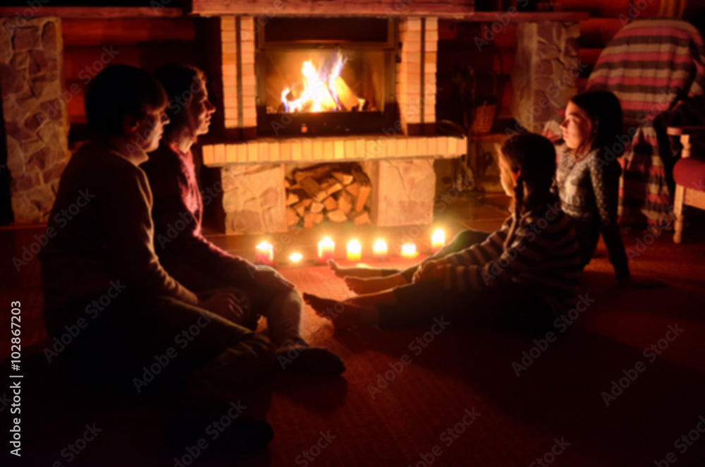 一家人坐在房子的壁炉旁，父母和孩子在炉火旁放松的模糊画面