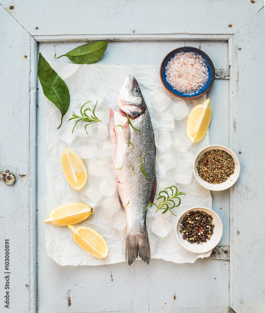 在质朴的蓝色木板背景上，用柠檬、香草、冰和香料烹制的新鲜生鲈鱼