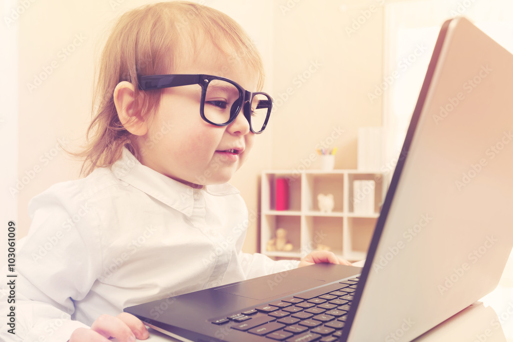 聪明的蹒跚学步的女孩戴着大眼镜用笔记本电脑