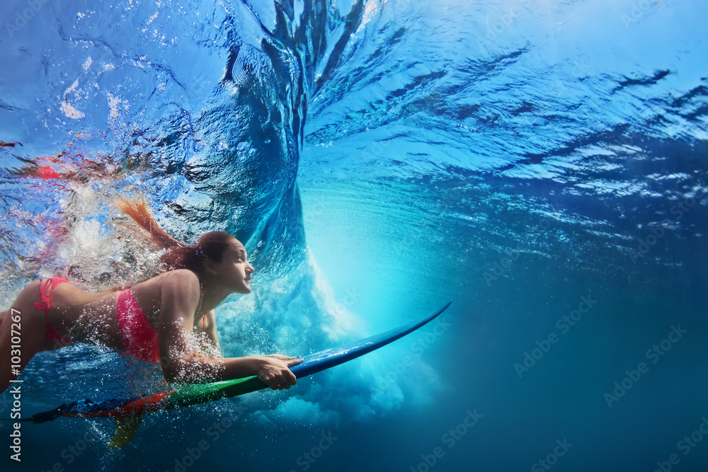 穿着比基尼的年轻女孩-冲浪者带着冲浪板在大浪下潜水家庭生活方式，