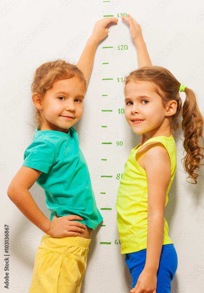两个女孩在家的墙上微笑显示身高