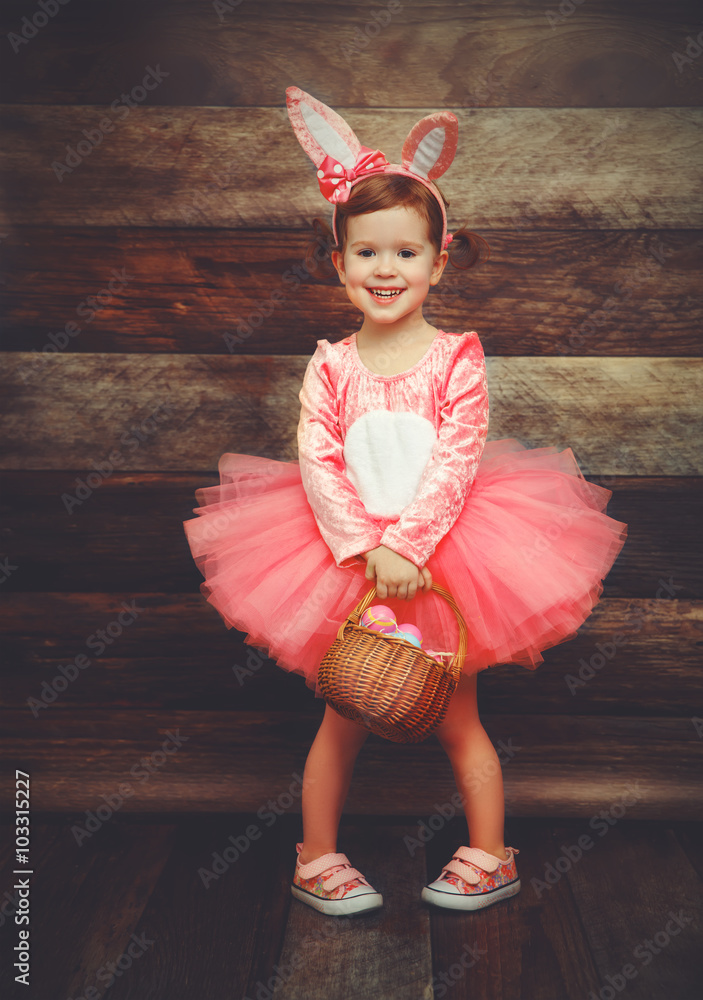 穿着戏服的快乐小女孩带篮子鸡蛋的复活节兔子