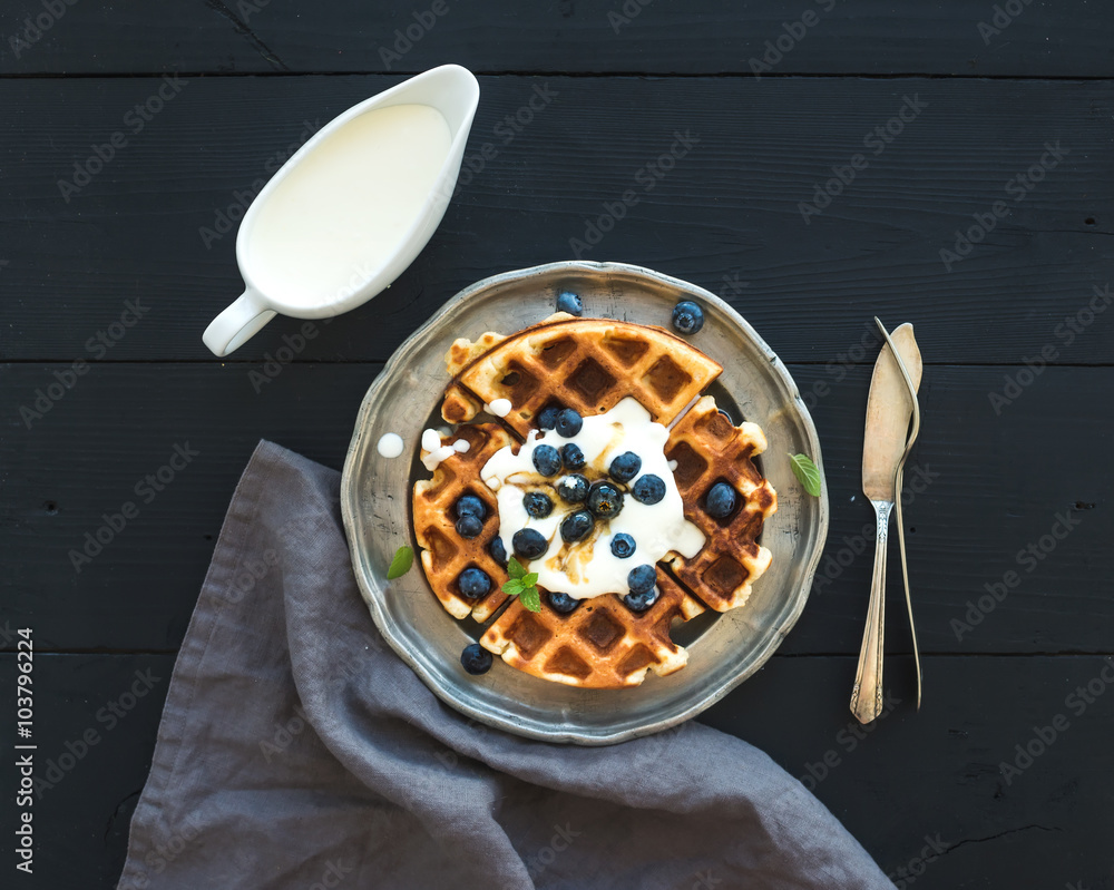 软比利时华夫饼，配蓝莓、蜂蜜和生奶油，放在复古金属盘上，配黑色woo
