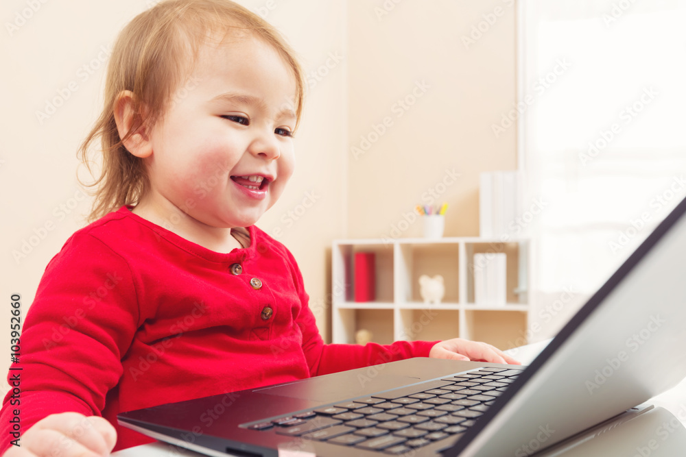 快乐的蹒跚学步的女孩在她的笔记本电脑上