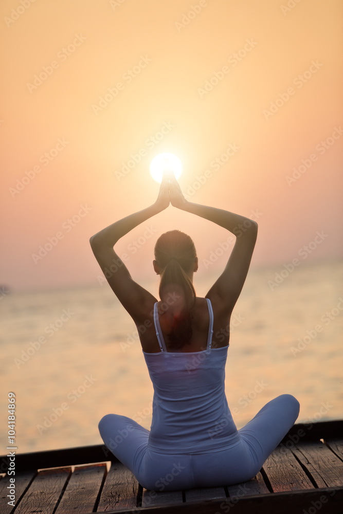 日落时在海滩上练习瑜伽的年轻女子