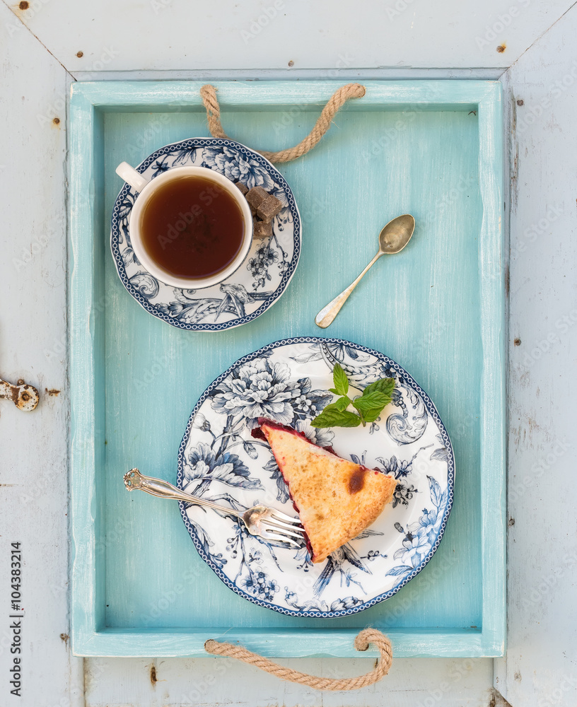 Piece of double crust plum pie and black tea in vintage porcelain cup, blue wooden tray. Top view .
