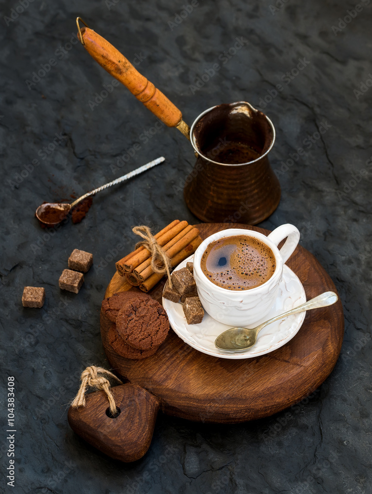 Cup of black coffee with chocolate biscuits, cinnamon sticks and cane sugar cubes on rustic wooden b