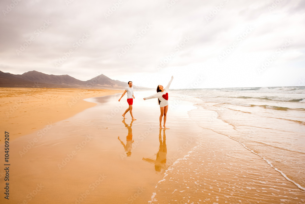 一对年轻夫妇在Fuertev上美丽的沙滩上跑步，沙滩背景是山脉，玩得很开心
