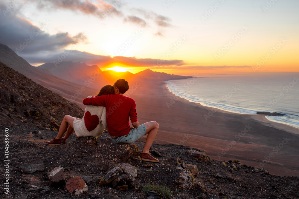 一对年轻夫妇坐在科菲特科的山上欣赏美丽的日落