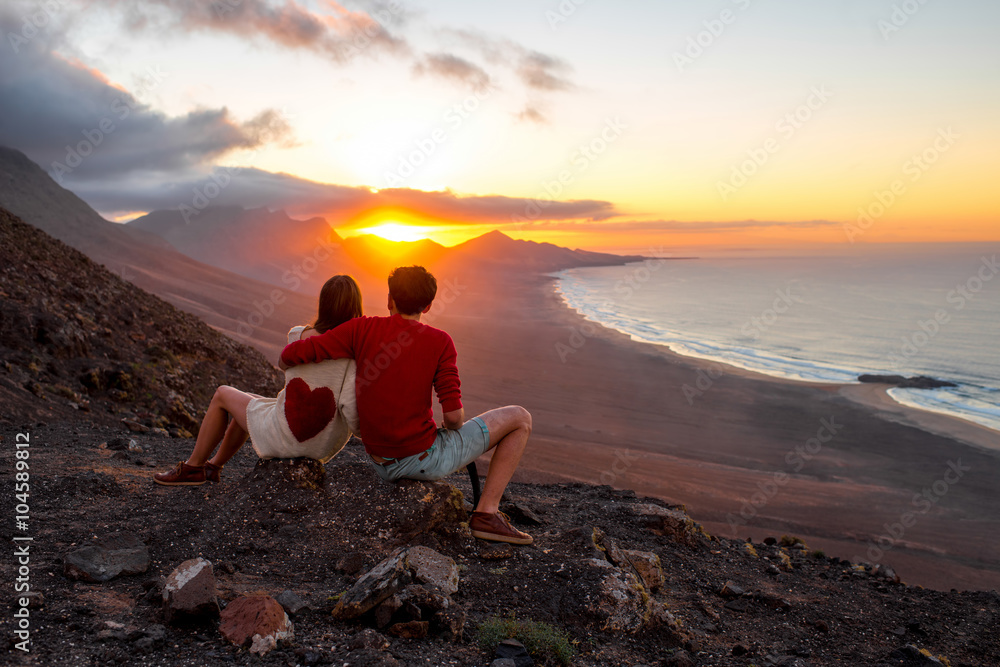一对年轻夫妇坐在科菲特科风景秀丽的山上欣赏美丽的日落