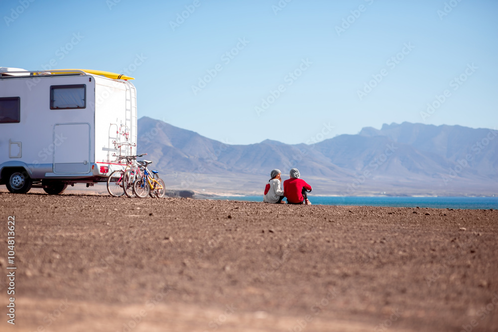 一对年轻夫妇坐在荒凉的海边露营拖车附近，背景是群山o